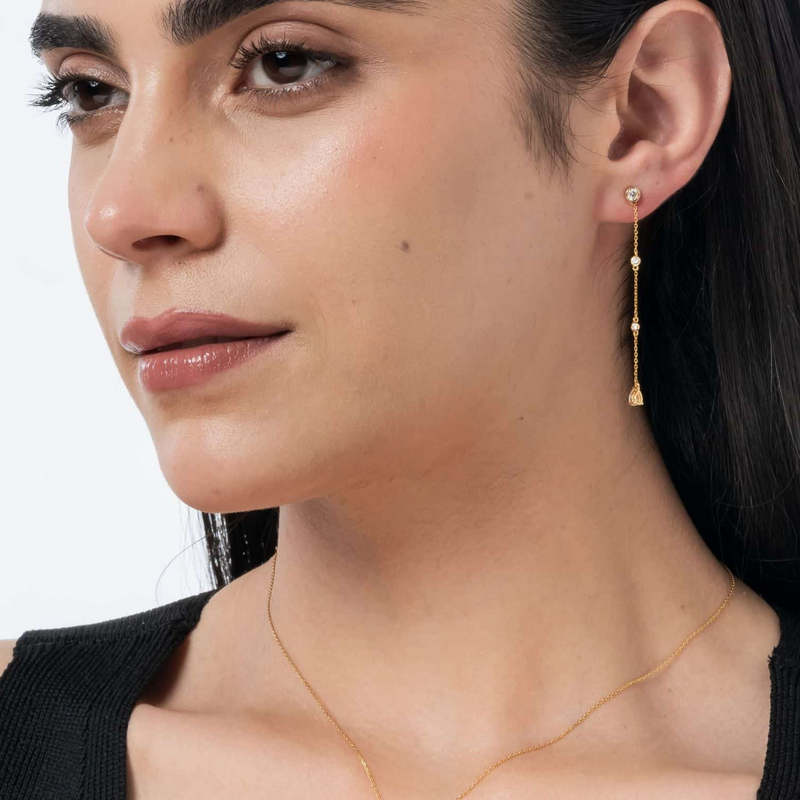 Close-up of a woman wearing gold earrings and a necklace against a neutral background